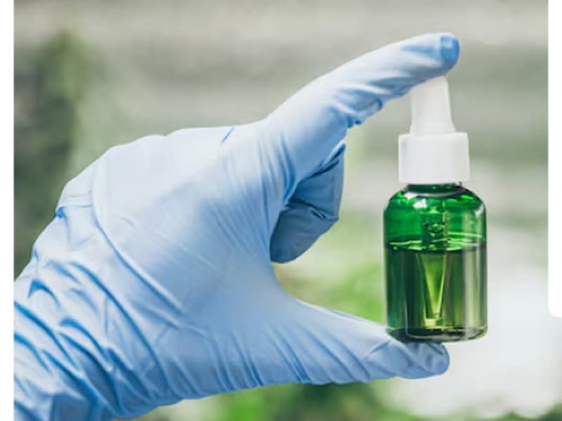 Gloved hand holding a green cosmetic dropper bottle